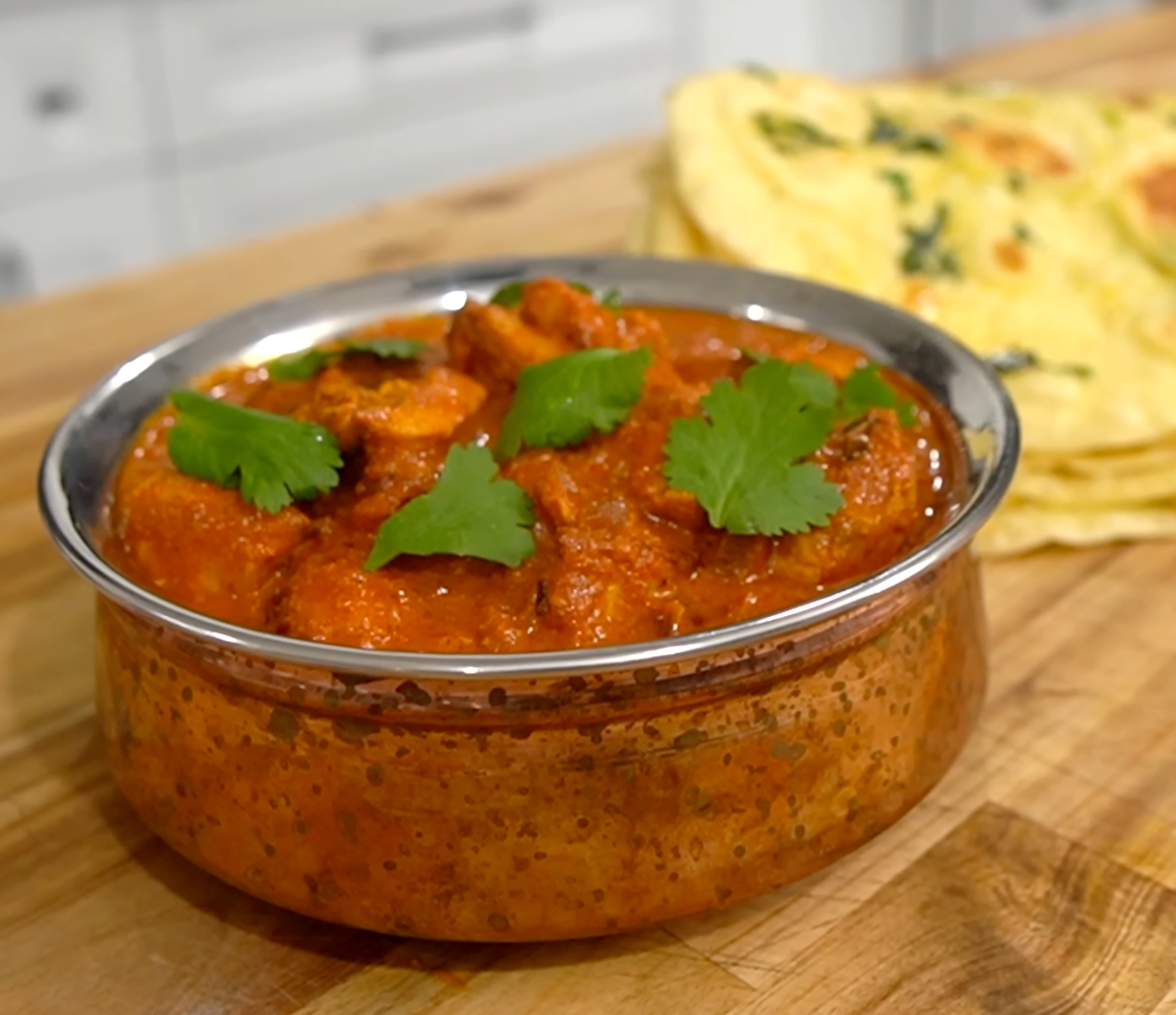 Chicken tikka masala v nerezovej miske, navrch čerstvý koriander a vedľa naan
